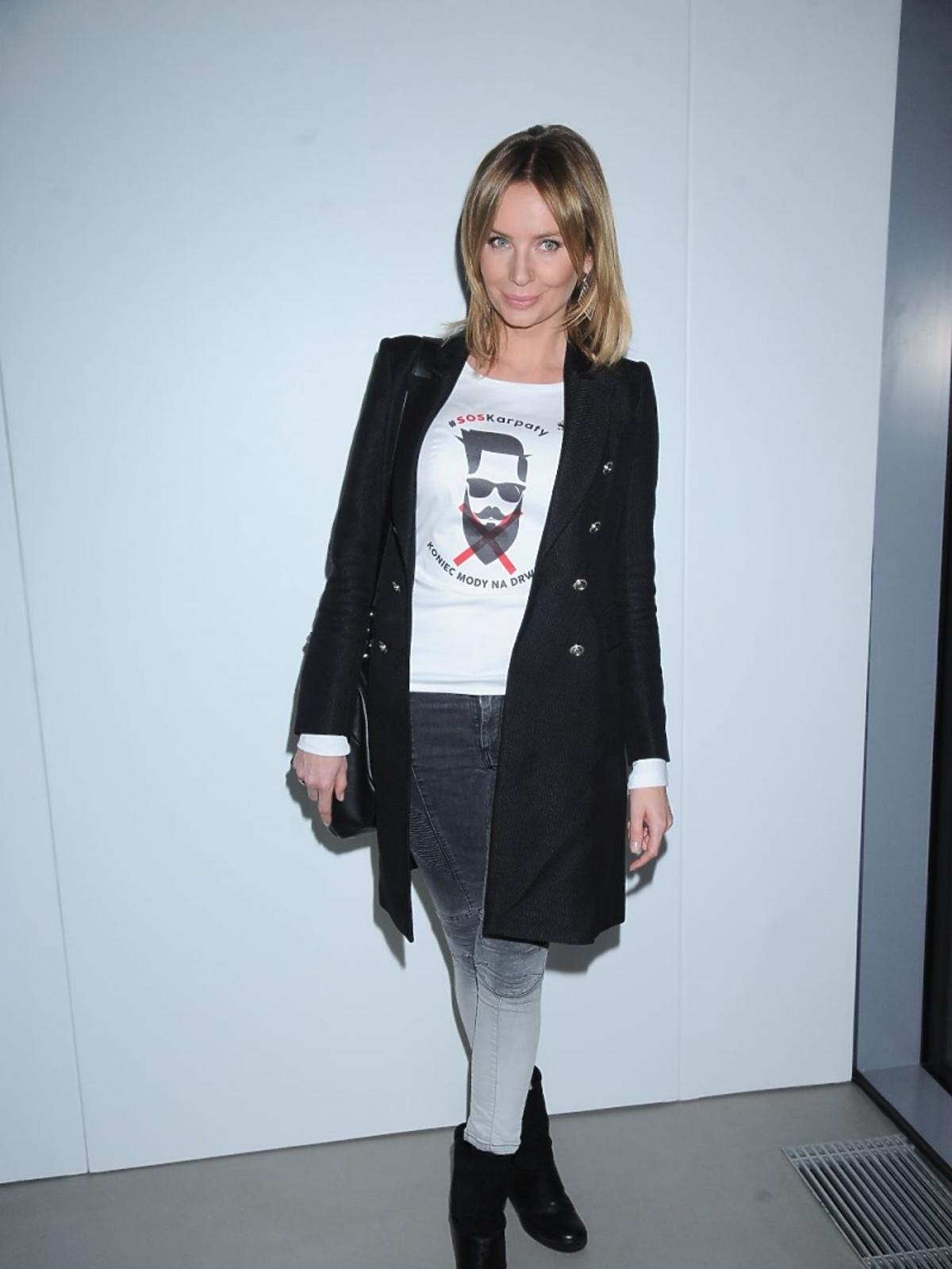 Agnieszka Szulim w czarnym płaszczu, białym T-shircie i szarych spodniach