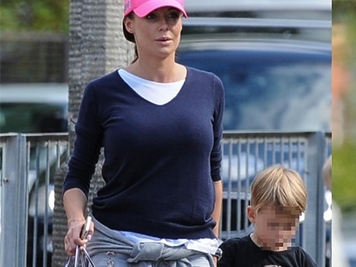 Małgorzata Rozenek w jasnych spodniach, białych butach, rózowej czapce na ulicy z synem