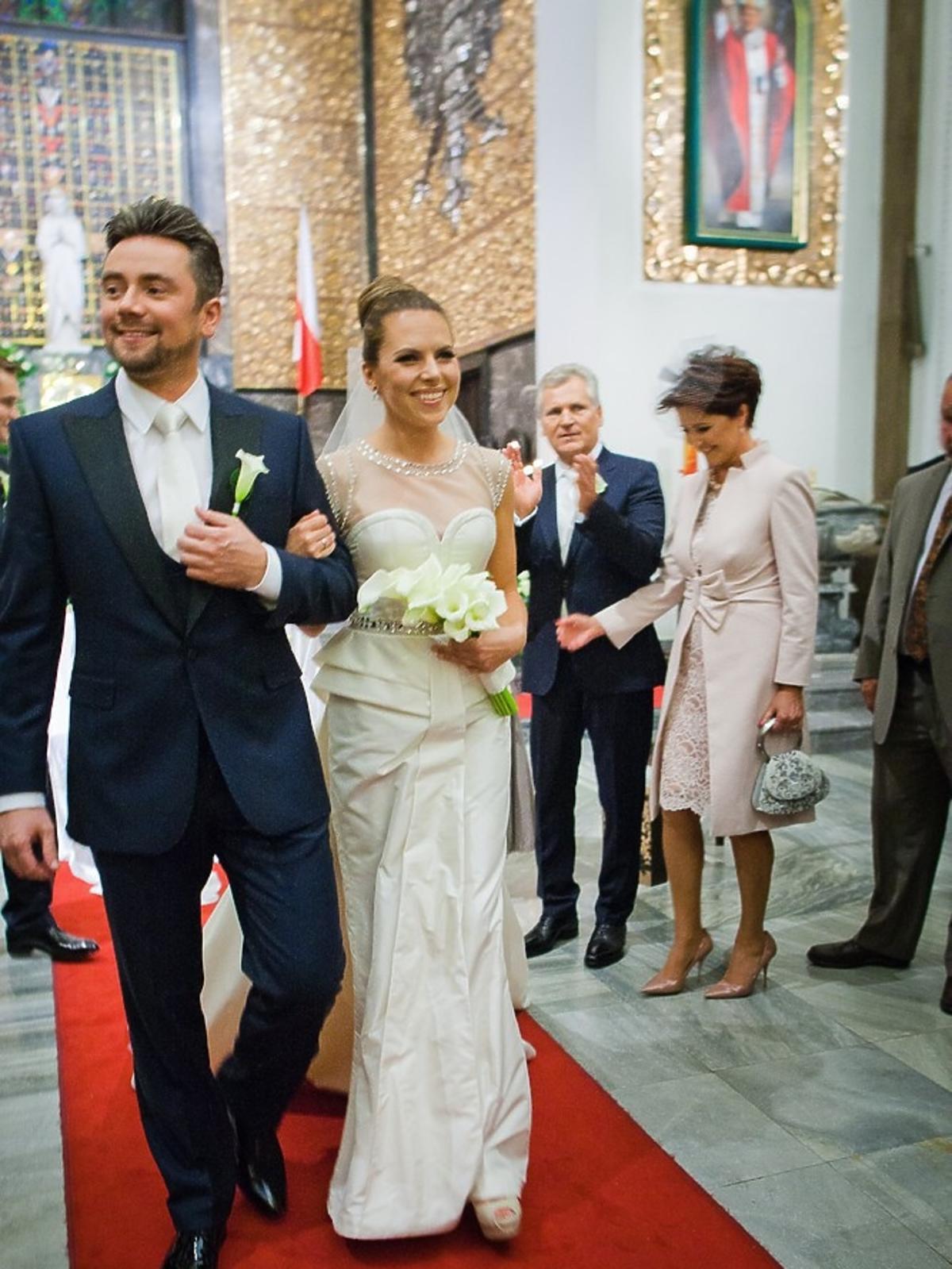 Aleksandra Kwaśniewska w białej sukni ślubnej idzie pod rękę z Kubą Badachem po czerwonym dywanie w kościele