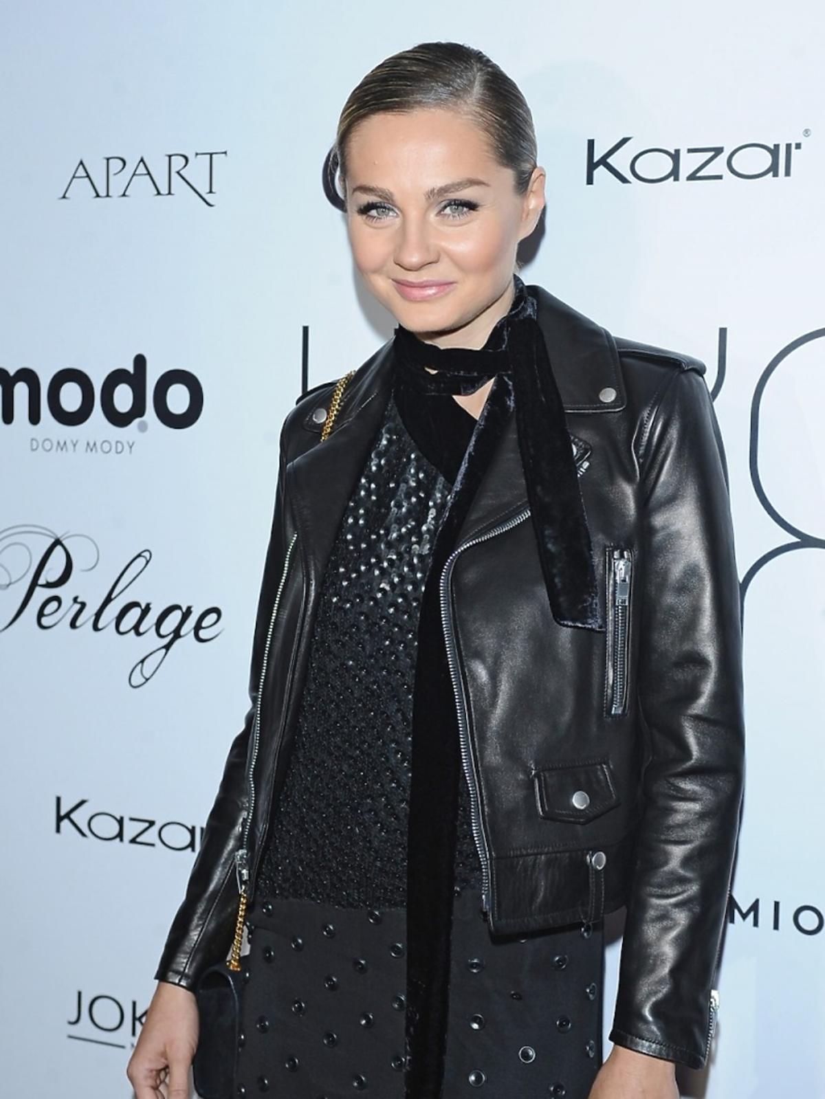 Małgorzata Socha w czarnej skórzanej kurtce, sukience, szaliku i szpilkach ze złotymi paskami