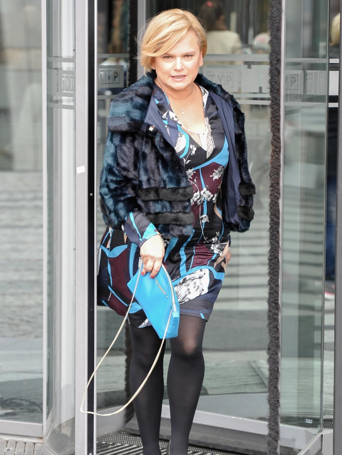 Katarzyna Figura w sukience w printy, kolorowym futerku, czarnych szpilkach i rajstopach, niebieską torebką
