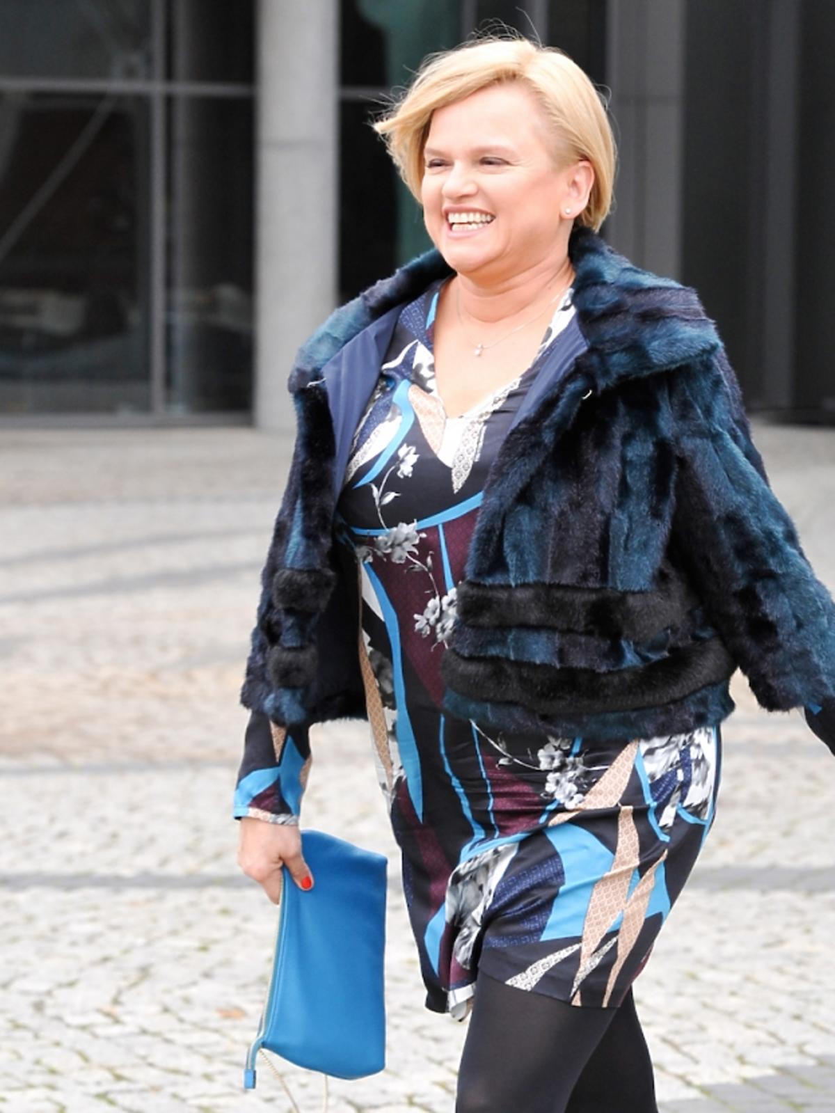 Katarzyna Figura w sukience w printy, kolorowym futerku, czarnych szpilkach i rajstopach, niebieską torebką