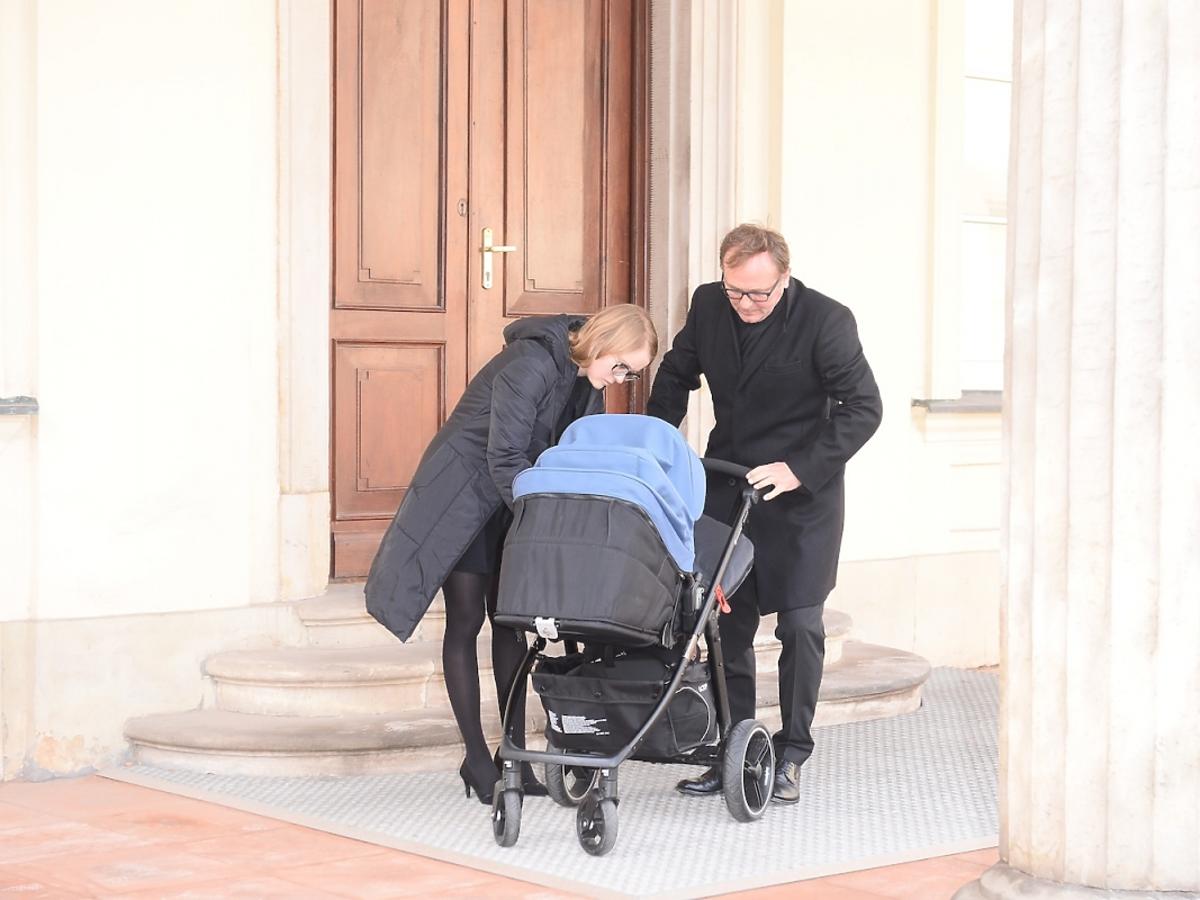 Andrzej Chyra w czarnym płaszczu z synkiem w niebieskim wózku i partnerką Pauliną przed ministerstwem