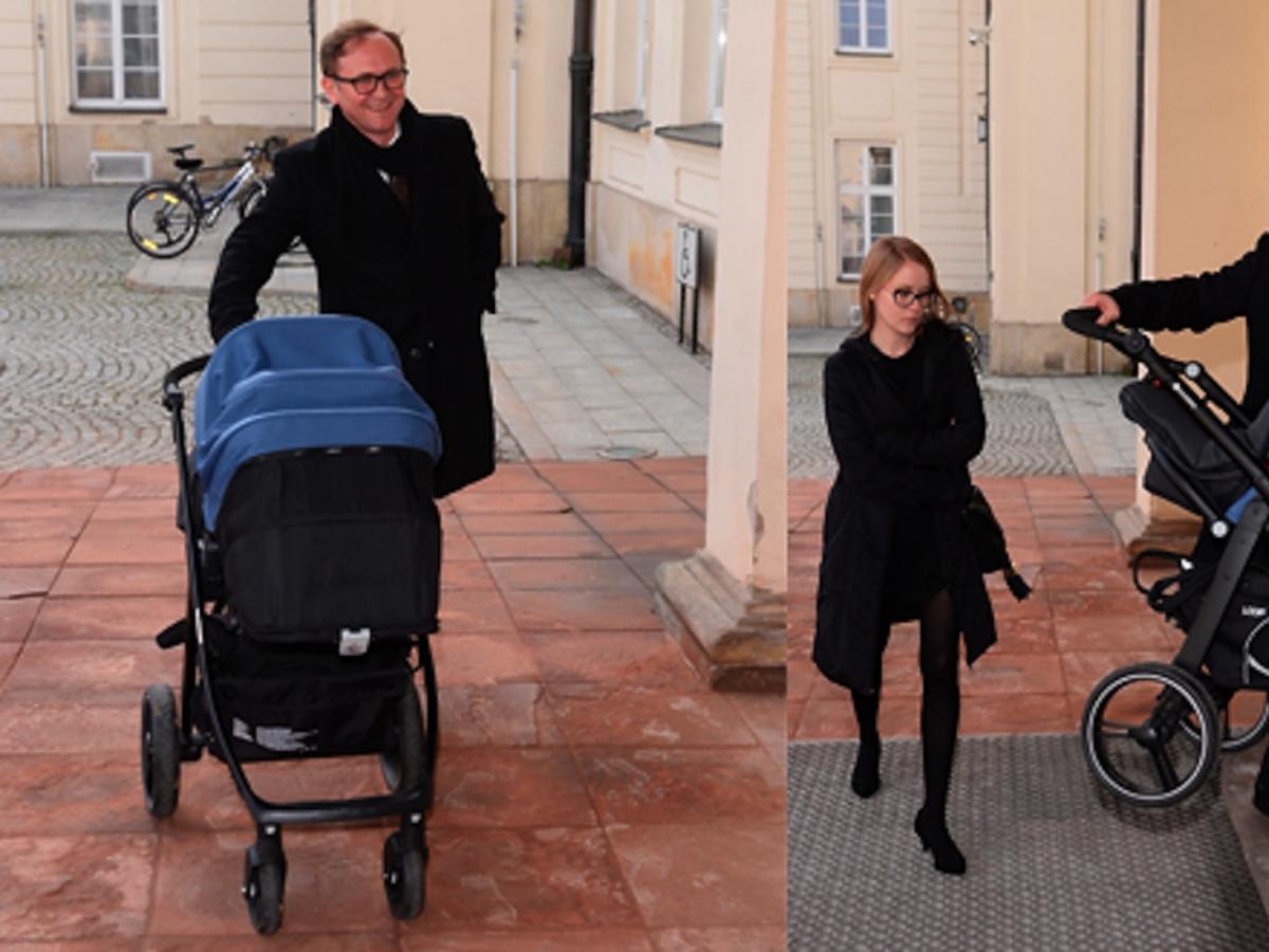 Andrzej Chyra w czarnym płaszczu z synkiem w wózku i partnerką Pauliną przed ministerstwem