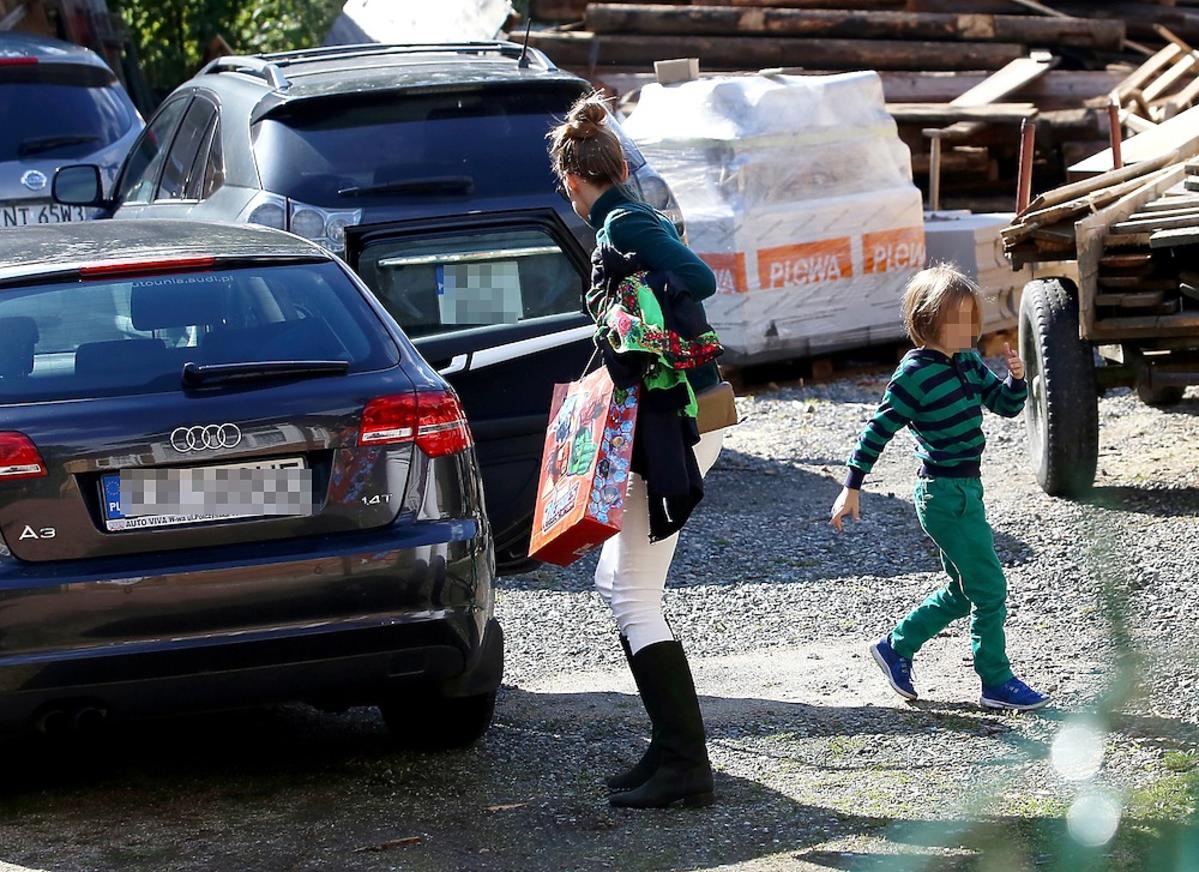 Alicha Bachleda-Curuś z upiętymi wlosami w kok i białych spodniach z synem na parkingu