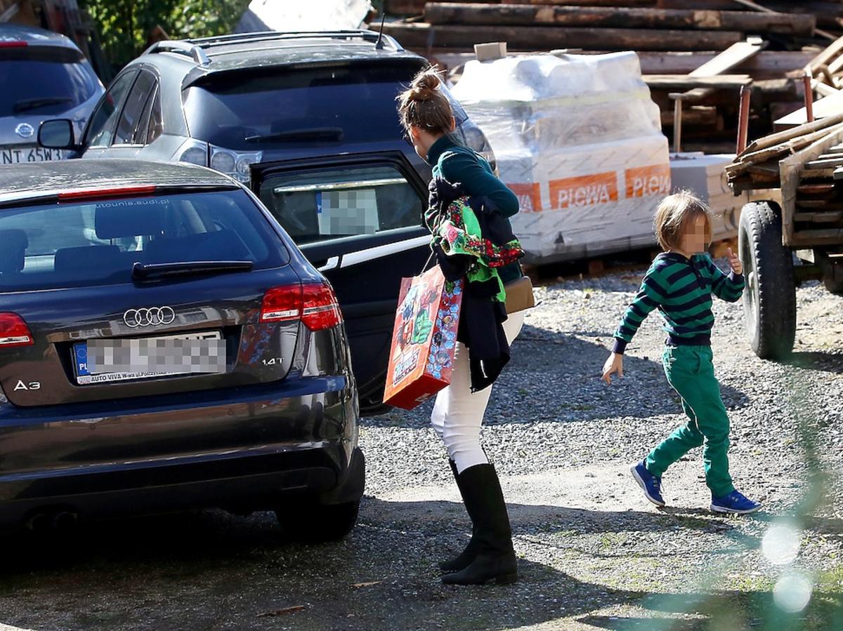 Alicha Bachleda-Curuś z upiętymi wlosami w kok i białych spodniach z synem na parkingu