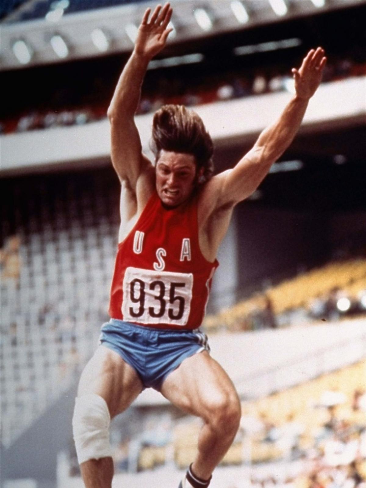 Bruce Jenner w trakcie skoku w dal, widać determinację na jego twarzy
