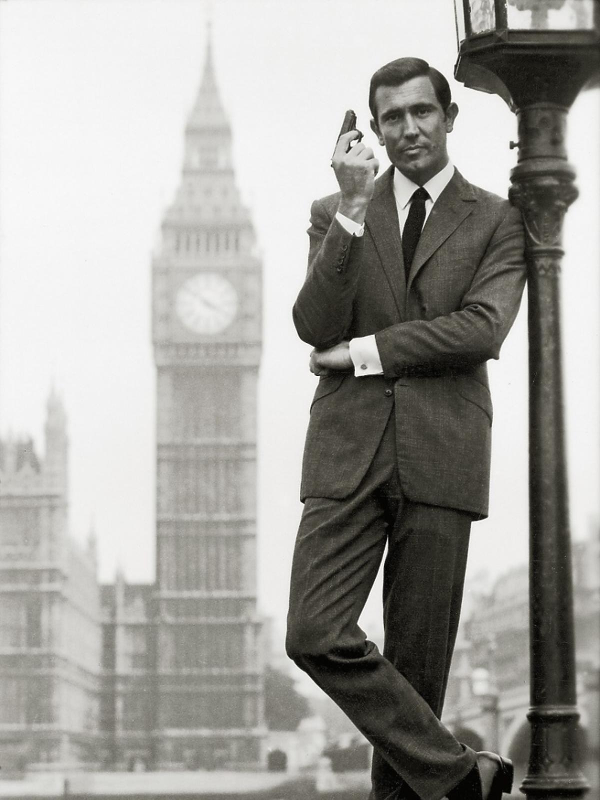George Lazenby w garniturze stoi oparty o lampę uliczną w tle widać Big Bena