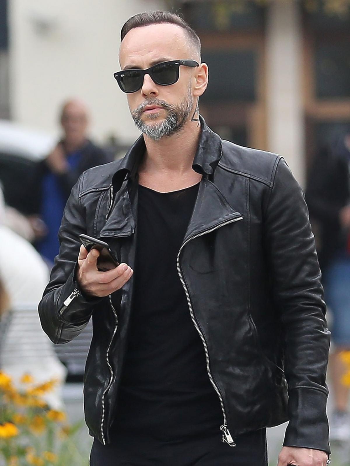 Nergal na ulicy w czarnej skórzanej kurtce, okularach przeciwsłonecznych trzyma w ręku telefon komórkowy