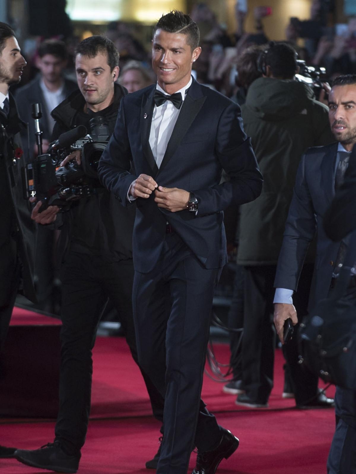 Uśmiechnięty elegancki Ronaldo w ganiturze i  w muszce zapina marynarkę