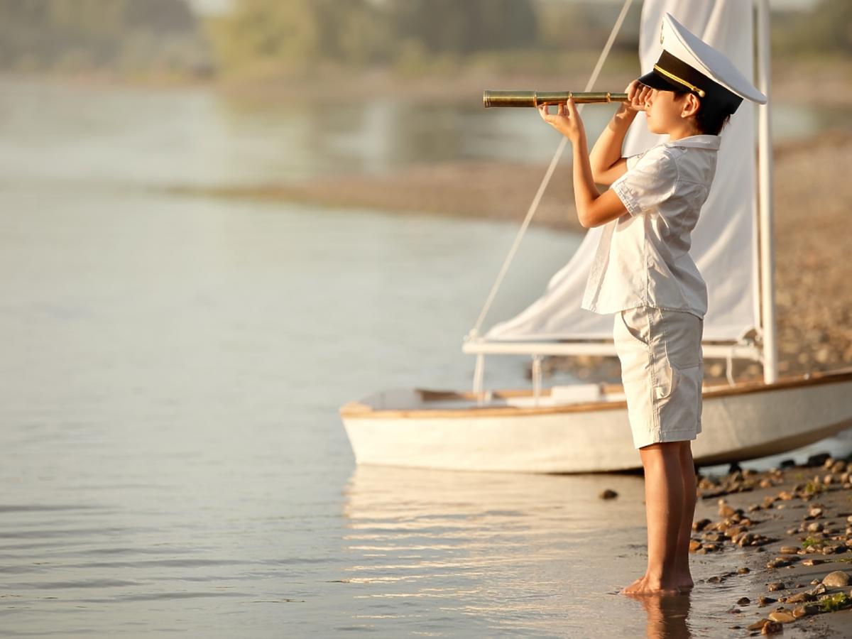 chłopiec w stroju marynarkim patrzy na morze przez lunetę