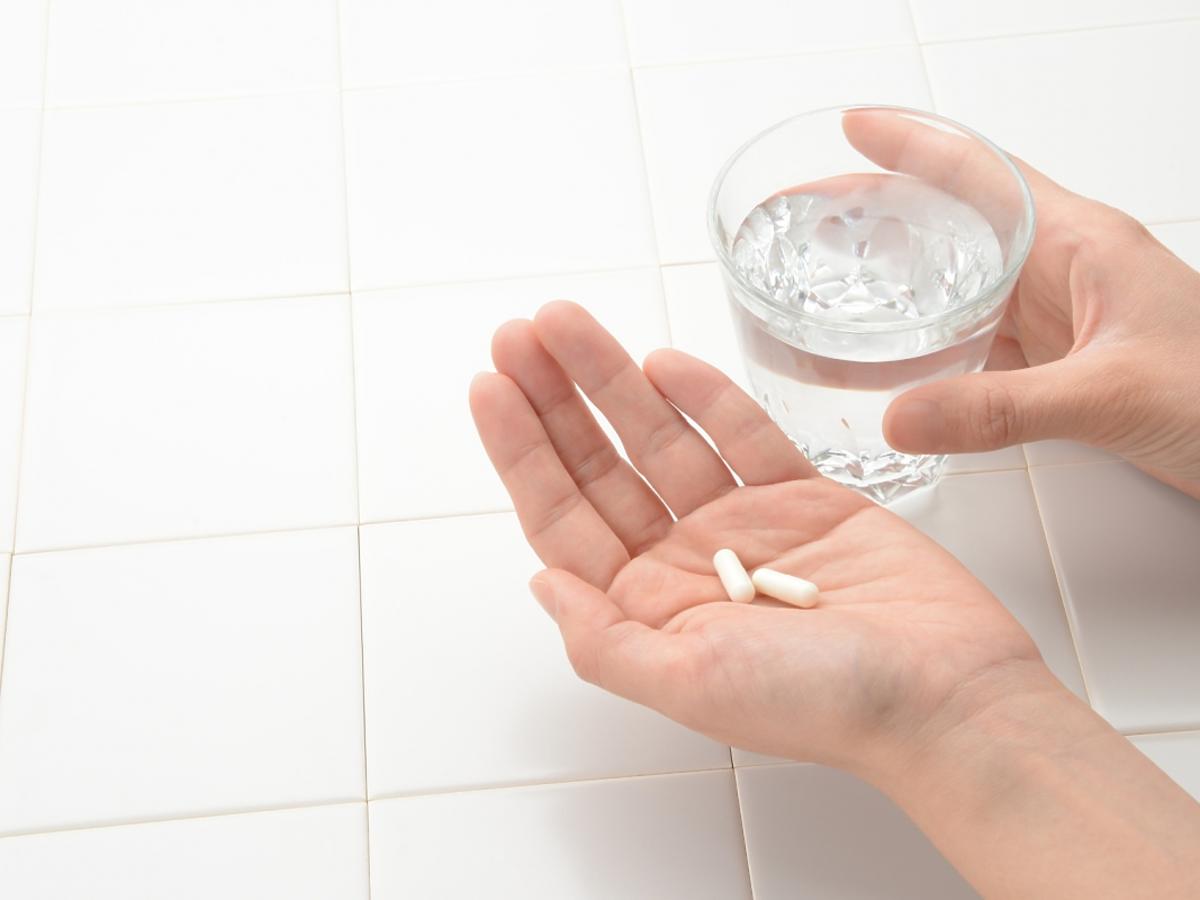 dłoń z tabletkami i szklanka wody
