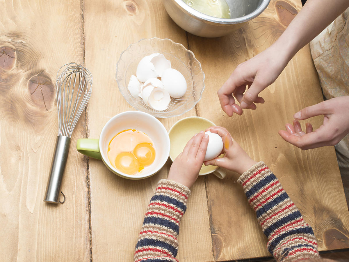 dłonie dwóch osób rozbijające jaja w miseczce