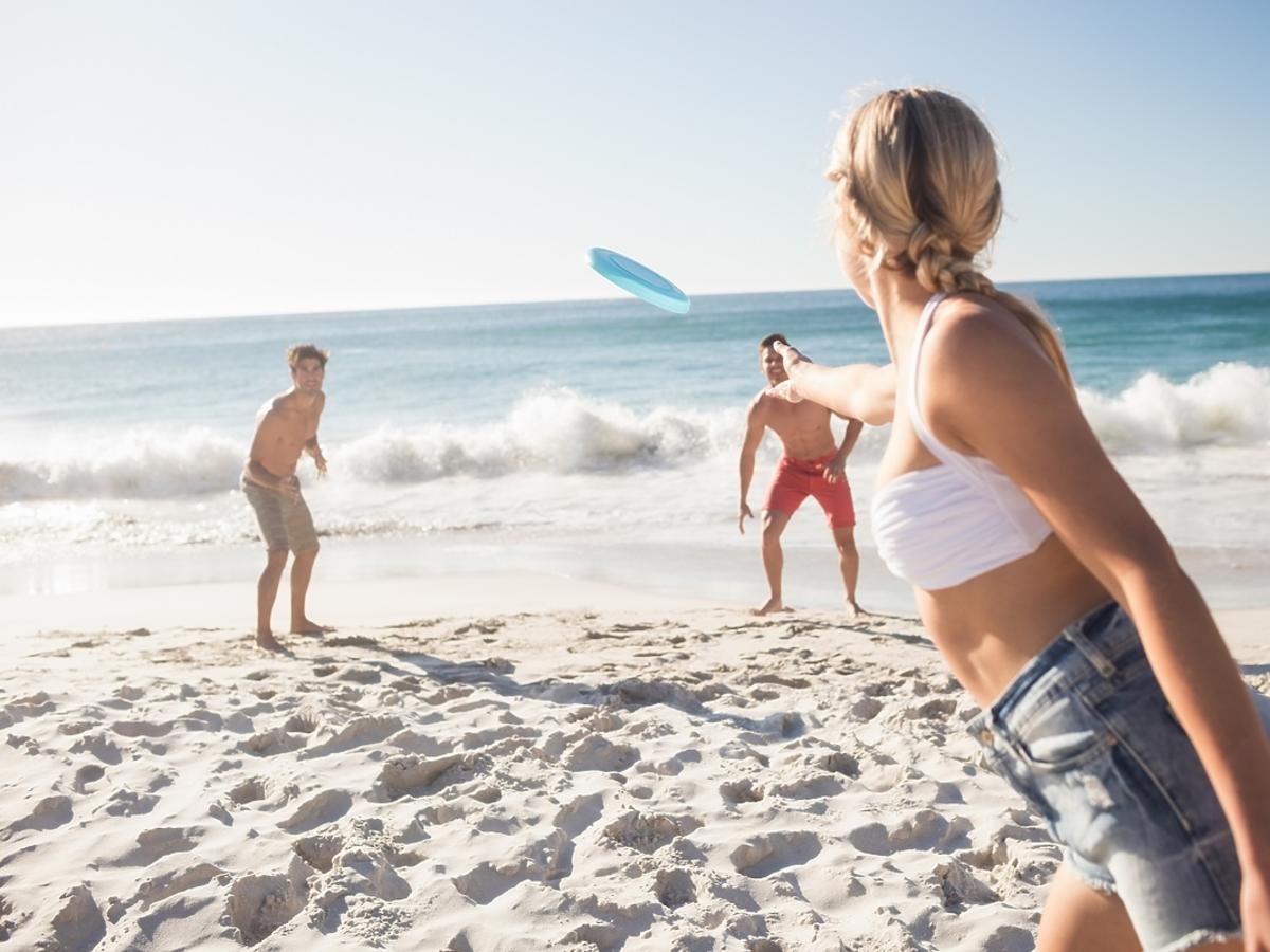Grupa przyjaciół gra w frisbee na plaży.