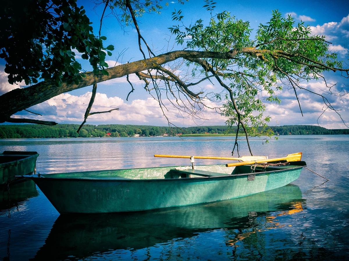 Jednoosobowa łódka przycumowana jest do mola na jeziorze.
