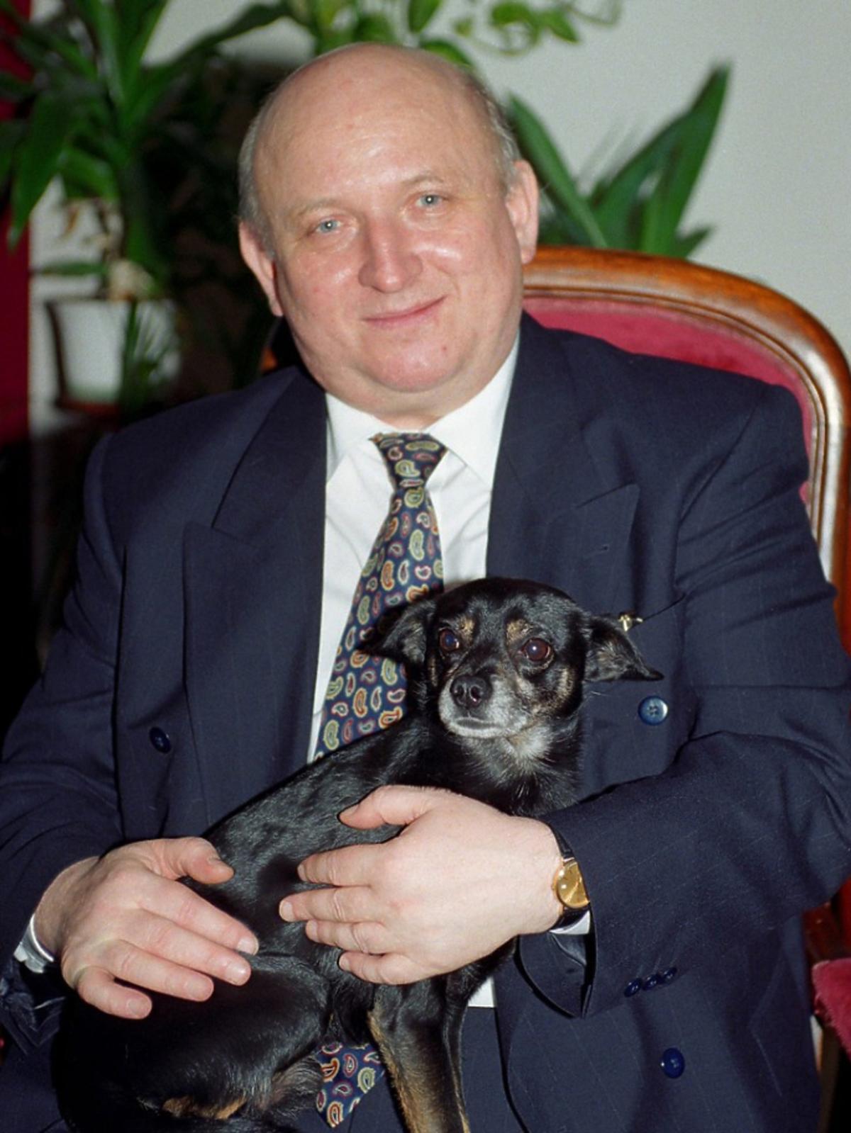 Józef Oleksy siedzi na fotelu z psem na kolanach, zdjęcie w domu