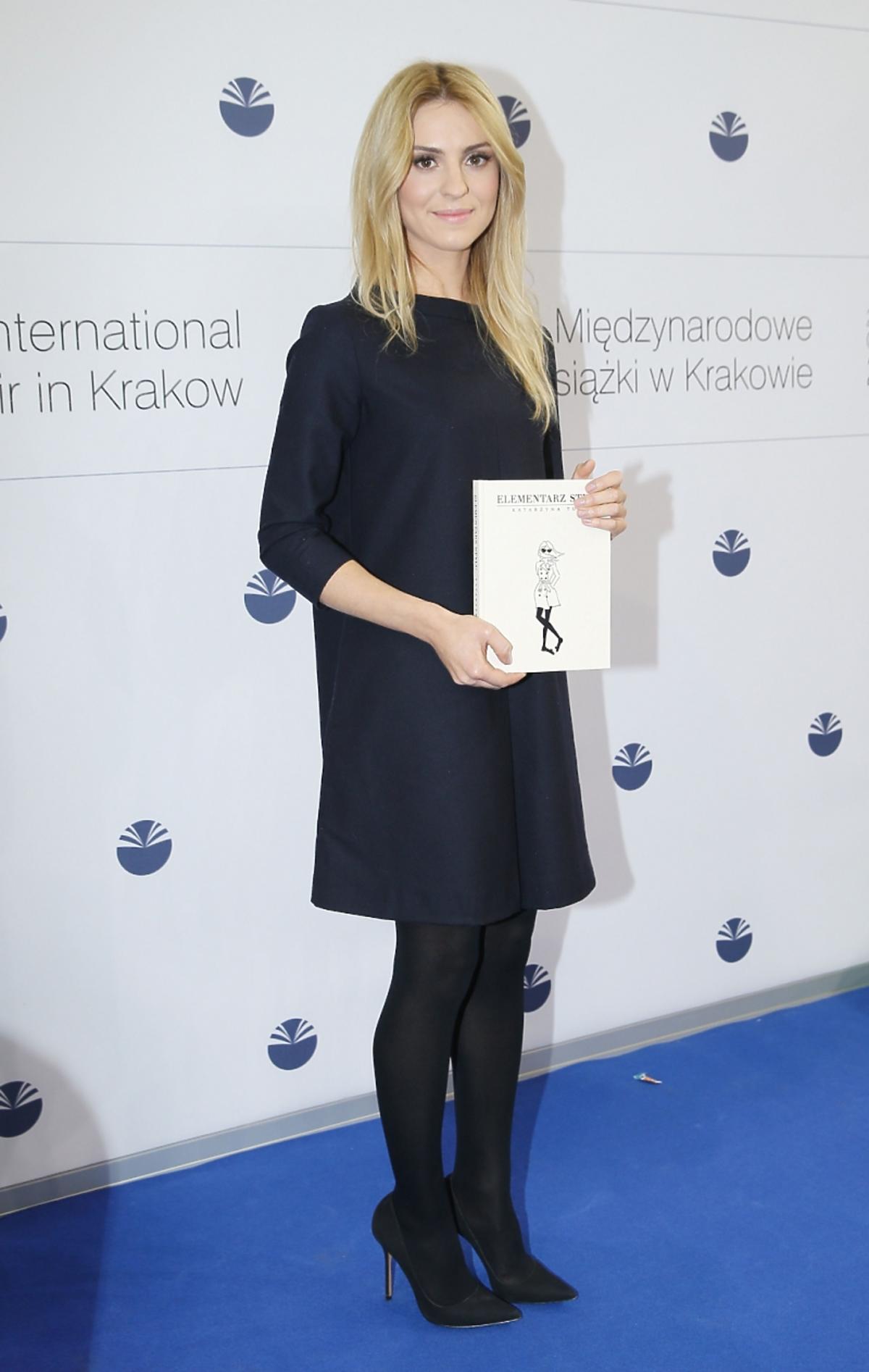 Kasia Tusk w czerni stoi na ściance na Targach Książki trzymając swoją książkę