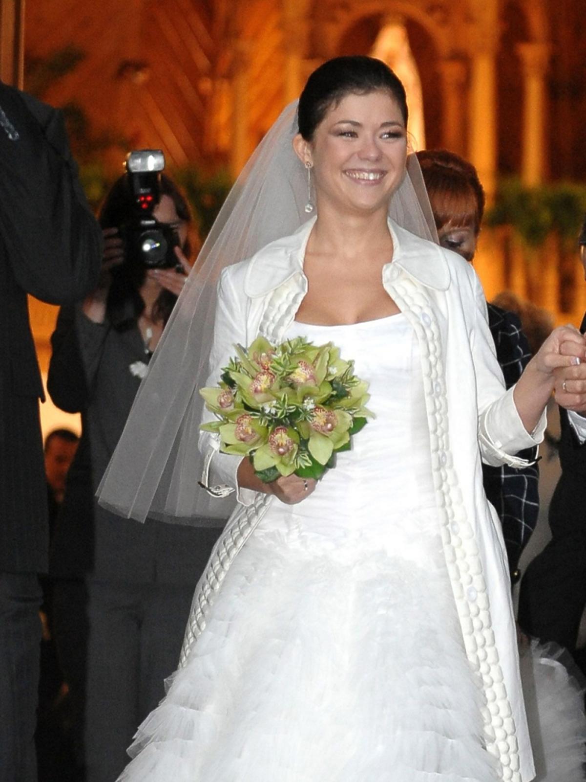 Katarzyna Cichopek w sukni ślubnej z welonem z bukietem kwiatów w wiszących kolczykach i w plaszczuku 