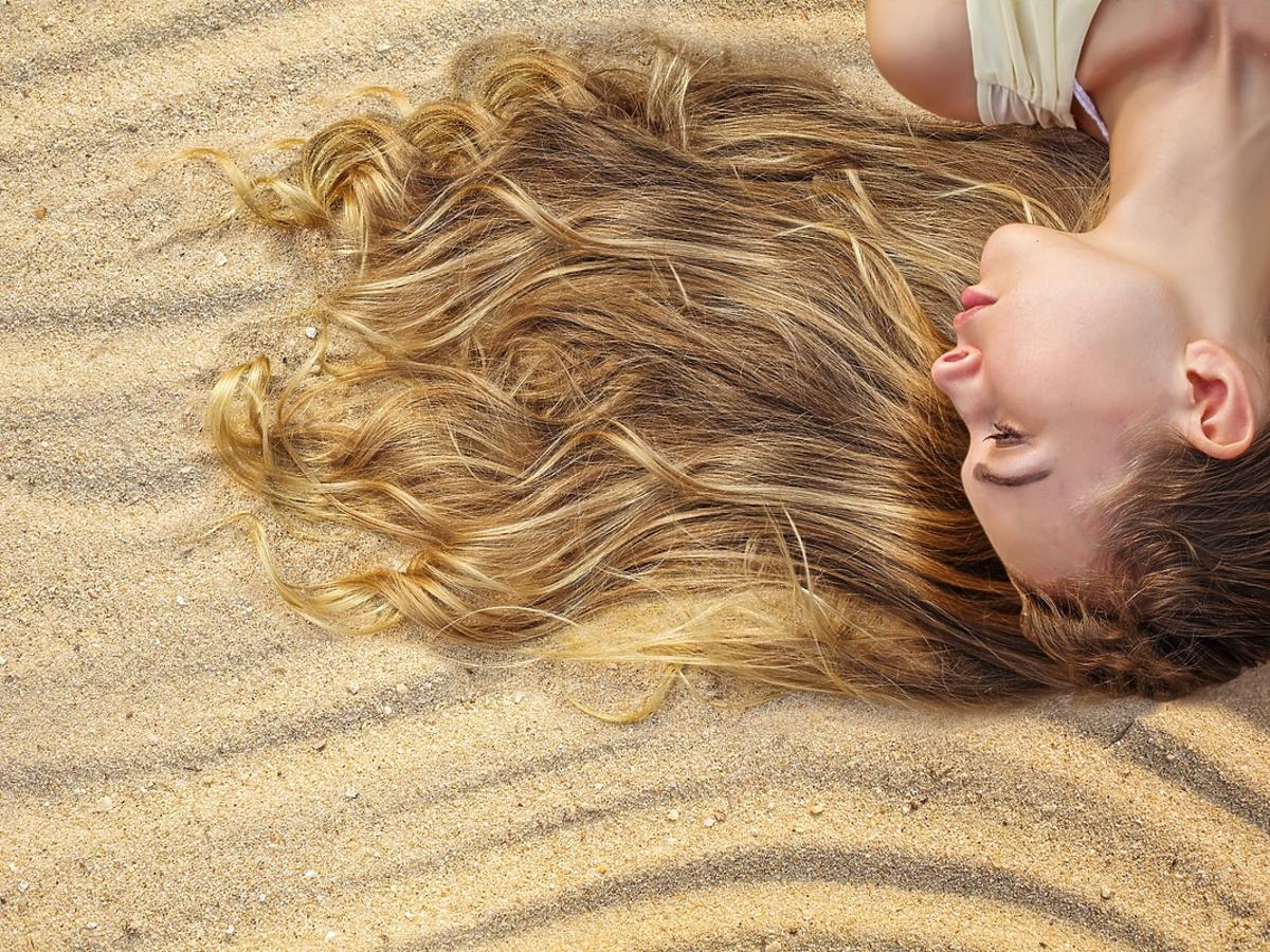 Kobieta o blond włosach leży na piaszczystej plaży.