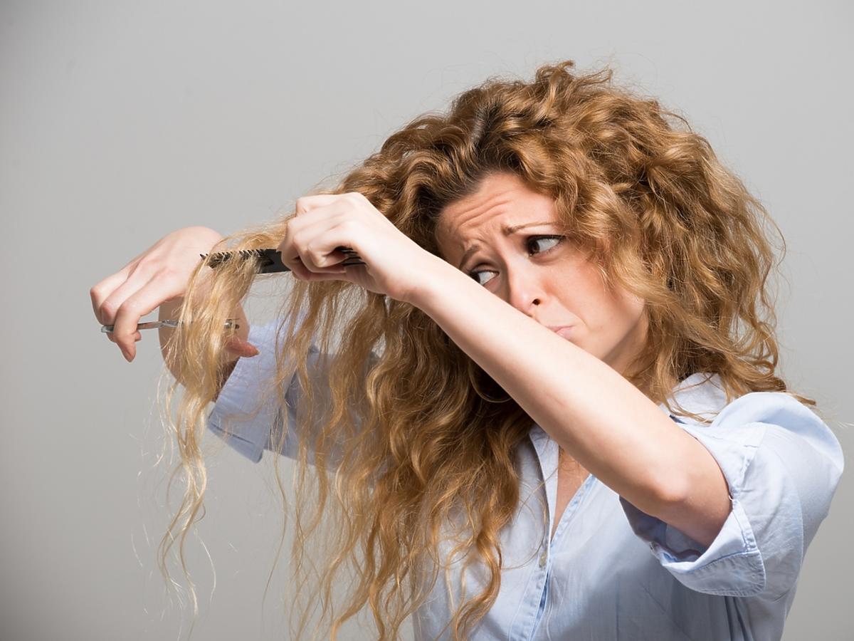 Kobieta o kręconych włosach rozczesuje niesforne kosmyki.
