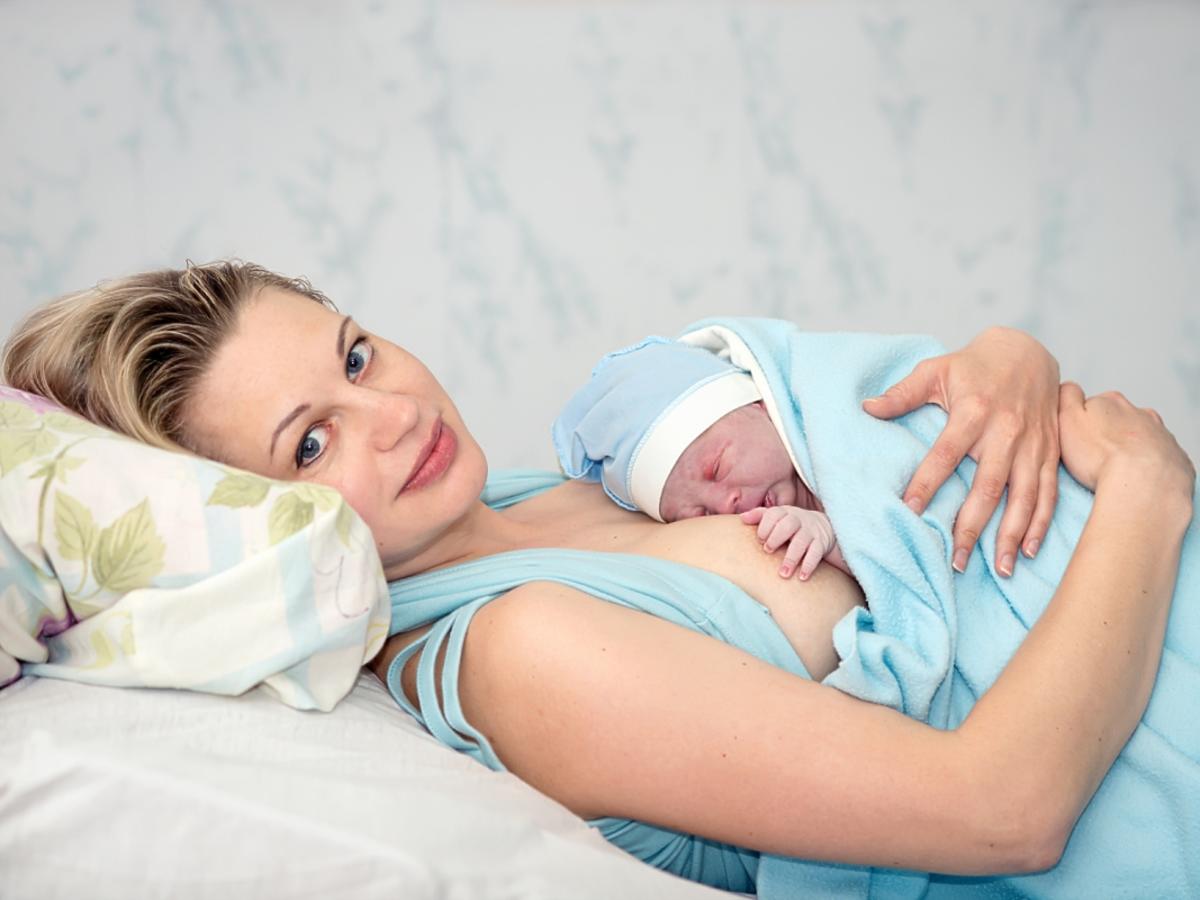 kobieta po porodzie leży z dzieckiem na łóżku