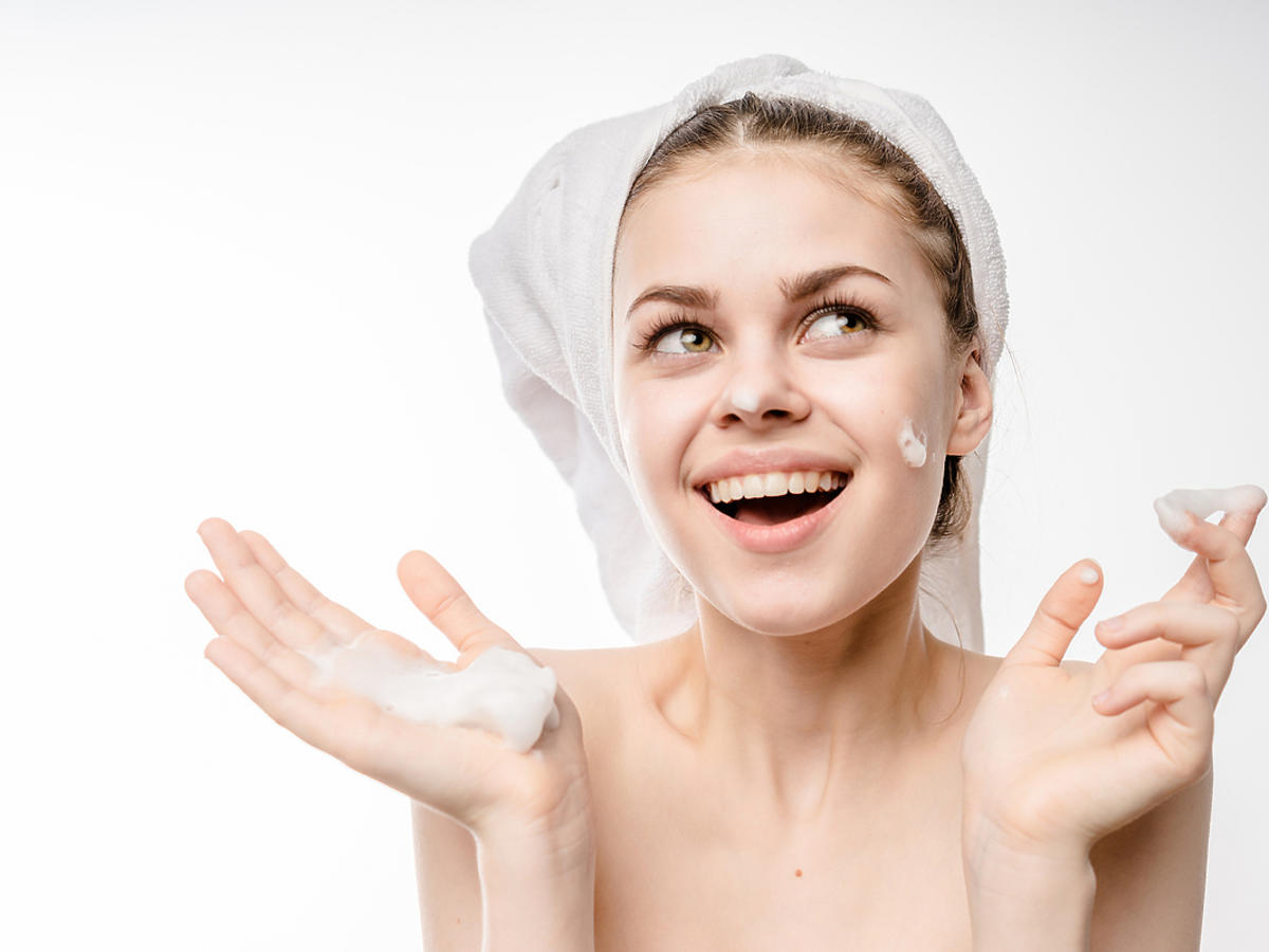 Kobieta stoi z ręcznikiem na głowie smaruje twarz kremem.