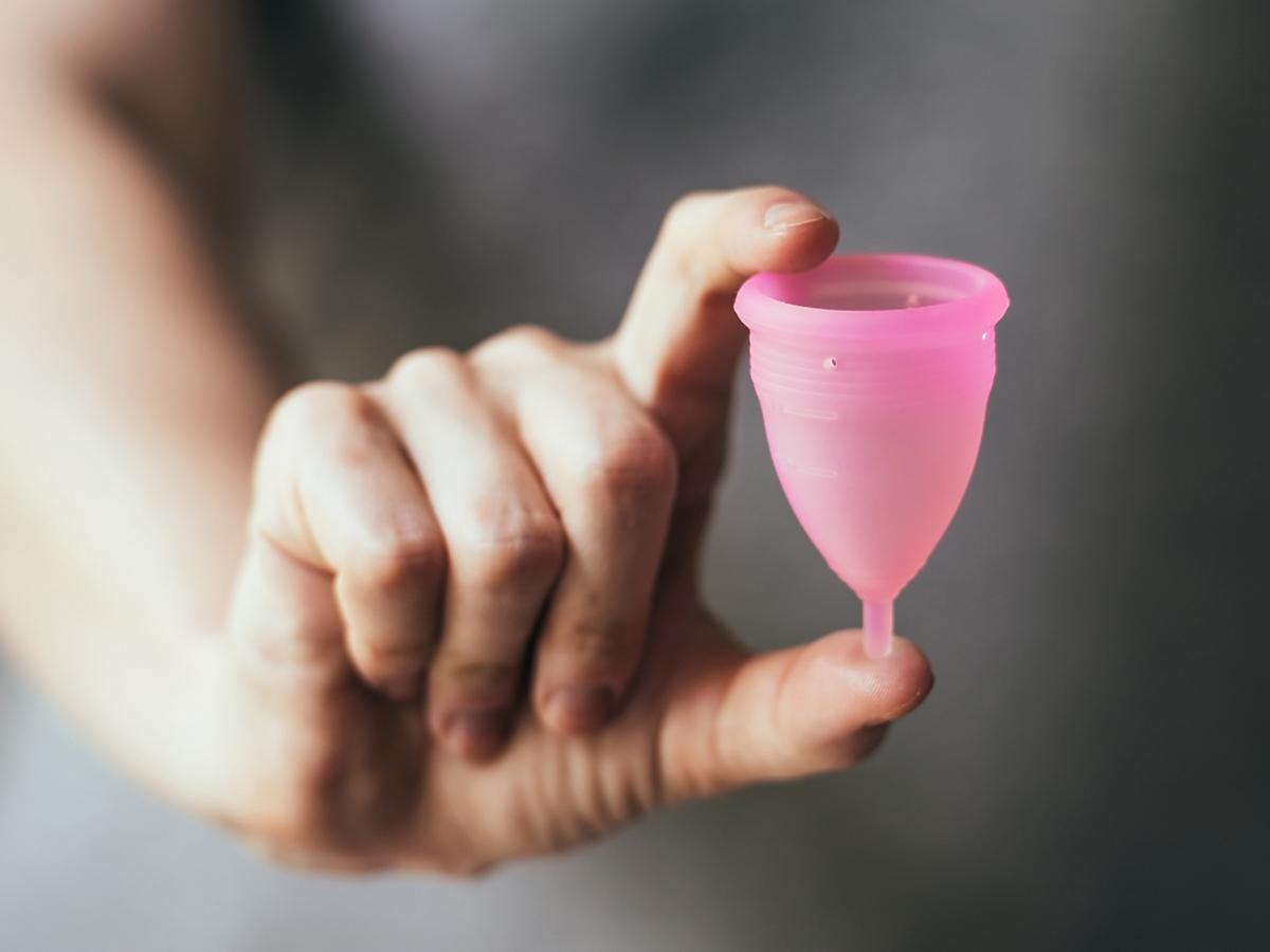 Kobieta trzyma w dłoni kubeczek menstruacyjny.