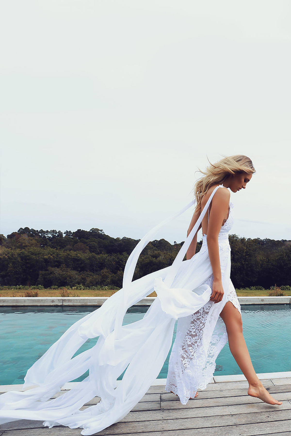 Kobieta w białej koronkowej sukni ślubnej z tiulem nad jeziorem
