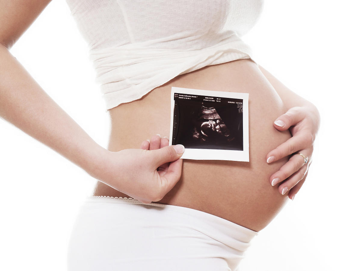 Kobieta w ciąży przykłada do brzucha zdjęcie USG.