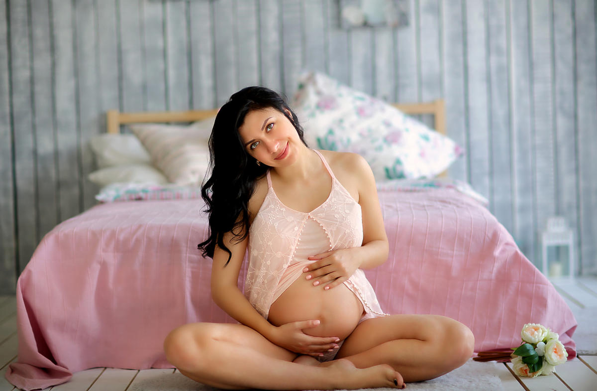 Kobieta w ciąży siedzi na dywanie i gładzi się po brzuchu