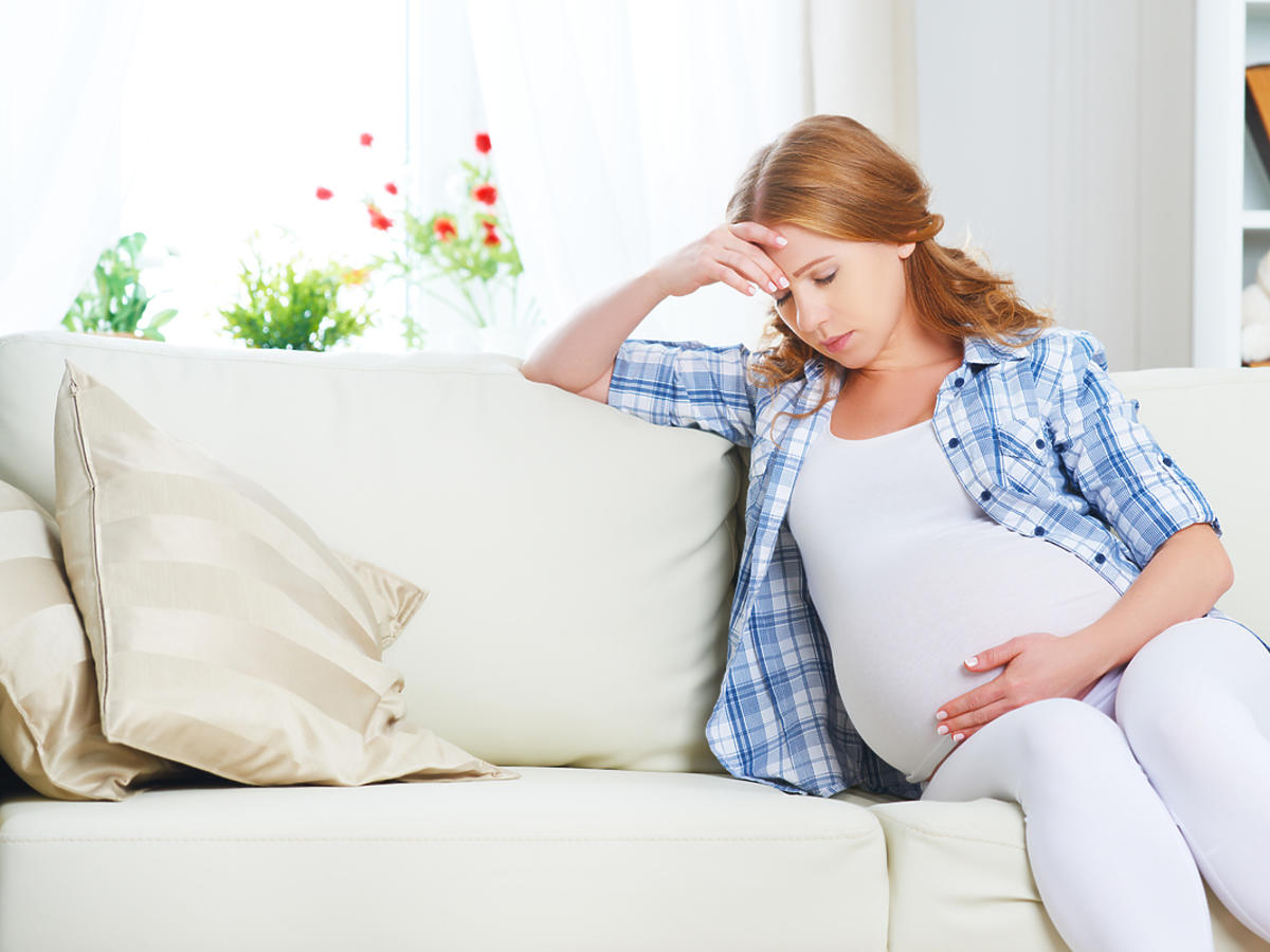 Kobieta w ciąży siedzi na kanapie, jest przygnębiona