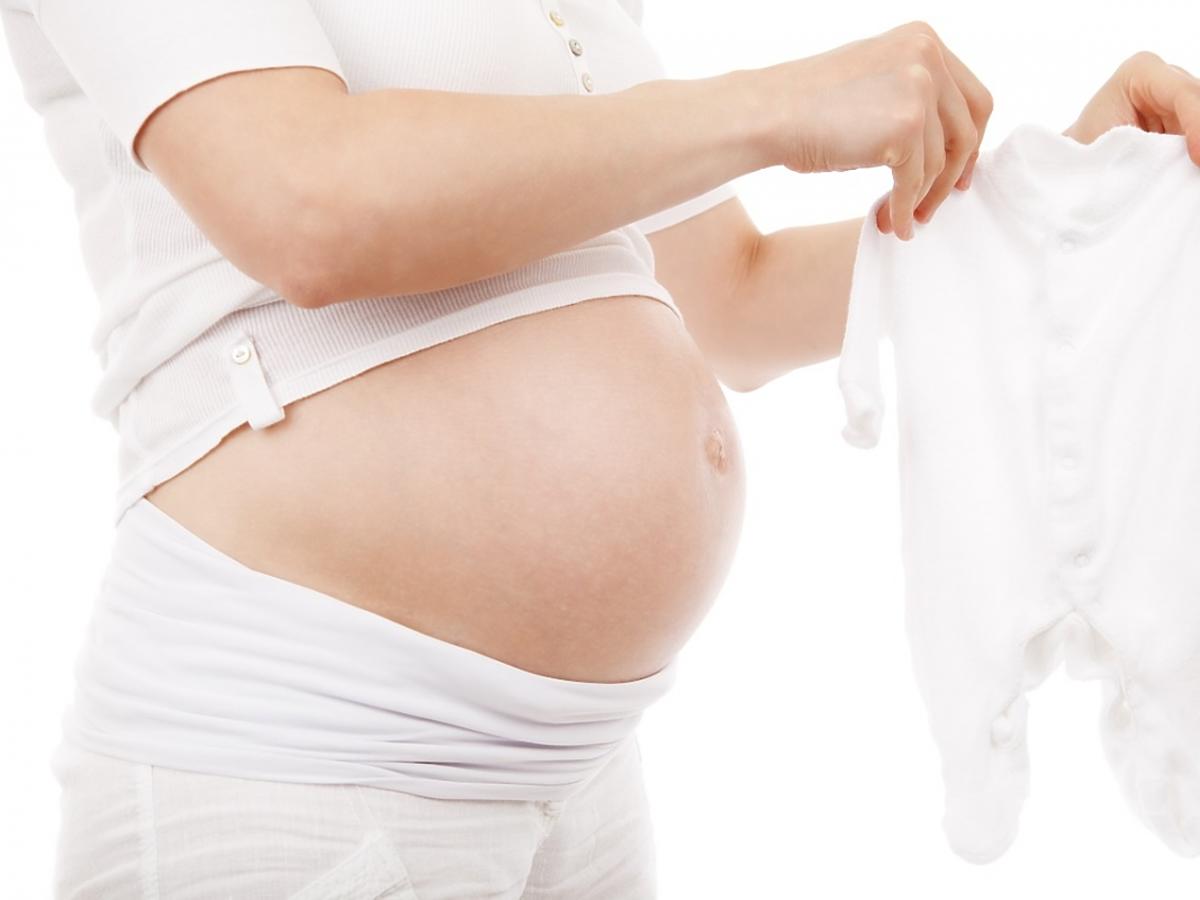 Kobieta w ciąży trzyma ubranko dla niemowlęcia