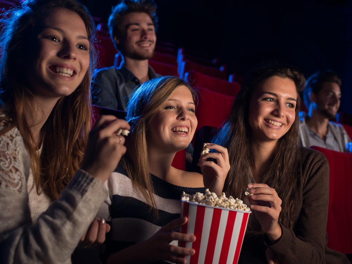 koleżanki oglądające film w kinie i jedzące popcorn