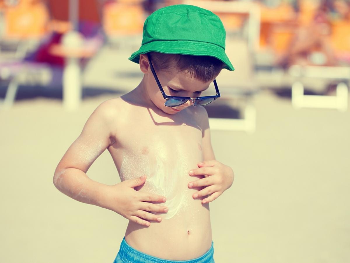 Mały chłopiec smaruje się kremem z filtrem na plaży.