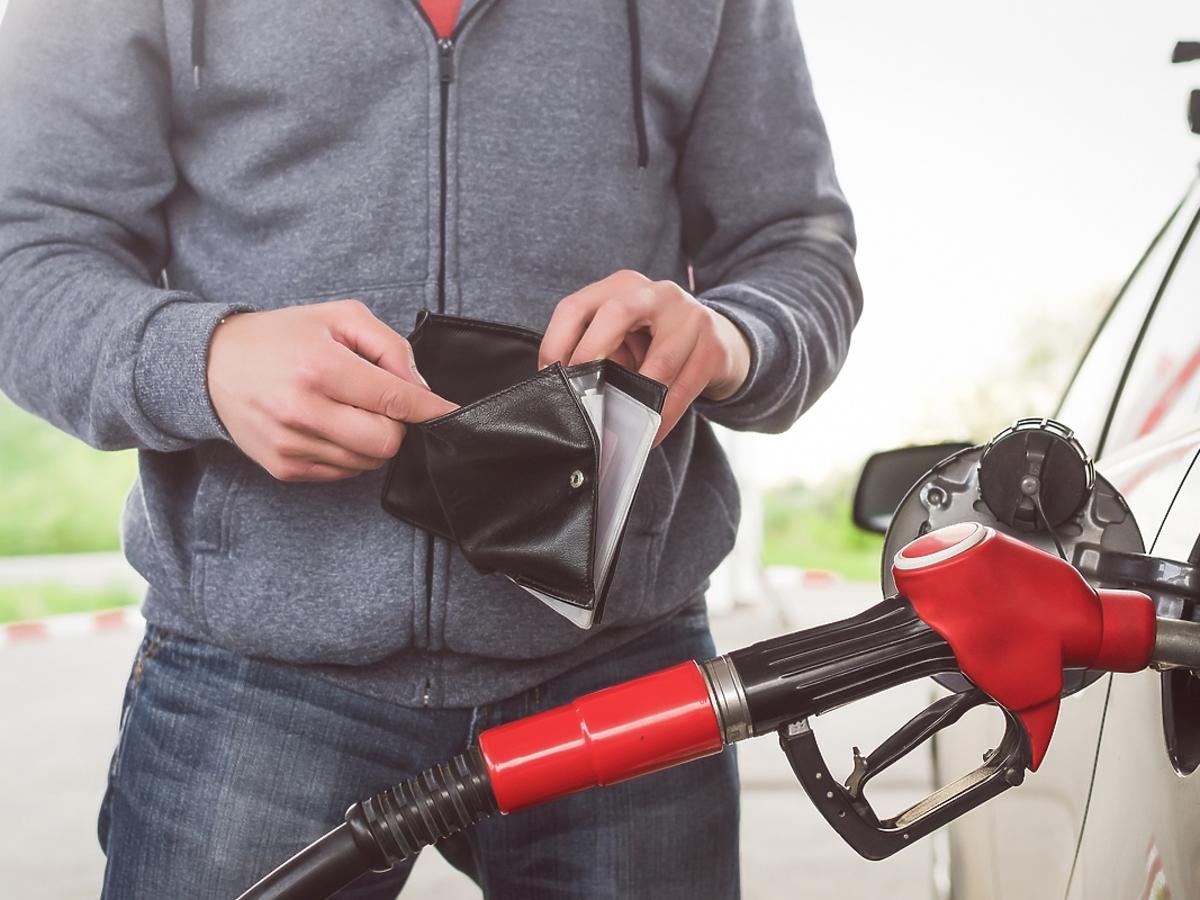 mężczyzna tankujący samochód na stacji benzynowej, trzymający portfel w dłoniach