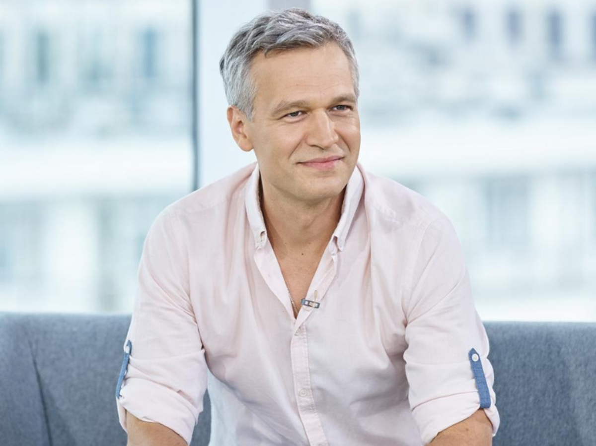 Michał Żebrowski siedzi na szarej kanapie