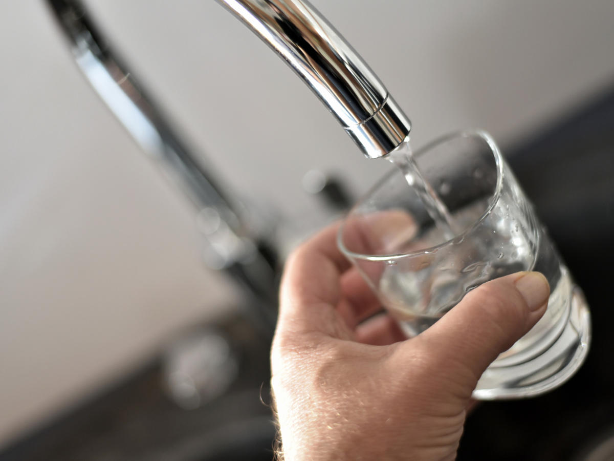 ręka trzymająca szklankę z wodą która leci z kranu