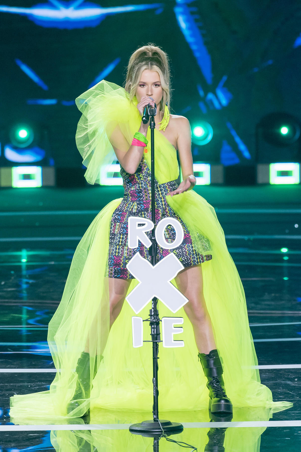 Roksana Węgiel na scene sopockiej Opery Leśnej, w zielonej sukience, śpiewa do mikrofonu z napisem Roxie