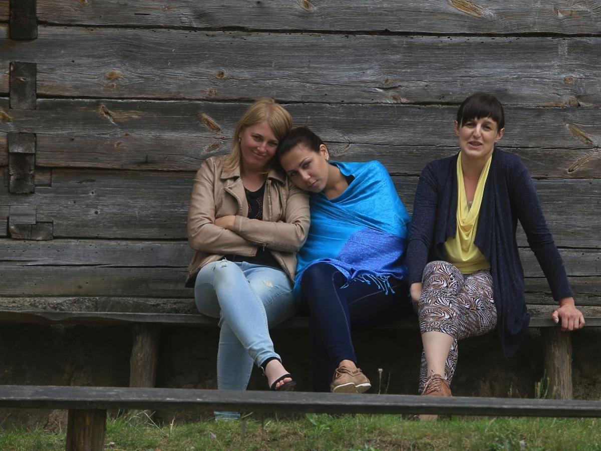 Krystyna, Joanna i Agnieszka w programie Rolnik szuka żony siedzą na drewnianej ławce przed drewnianą chatą