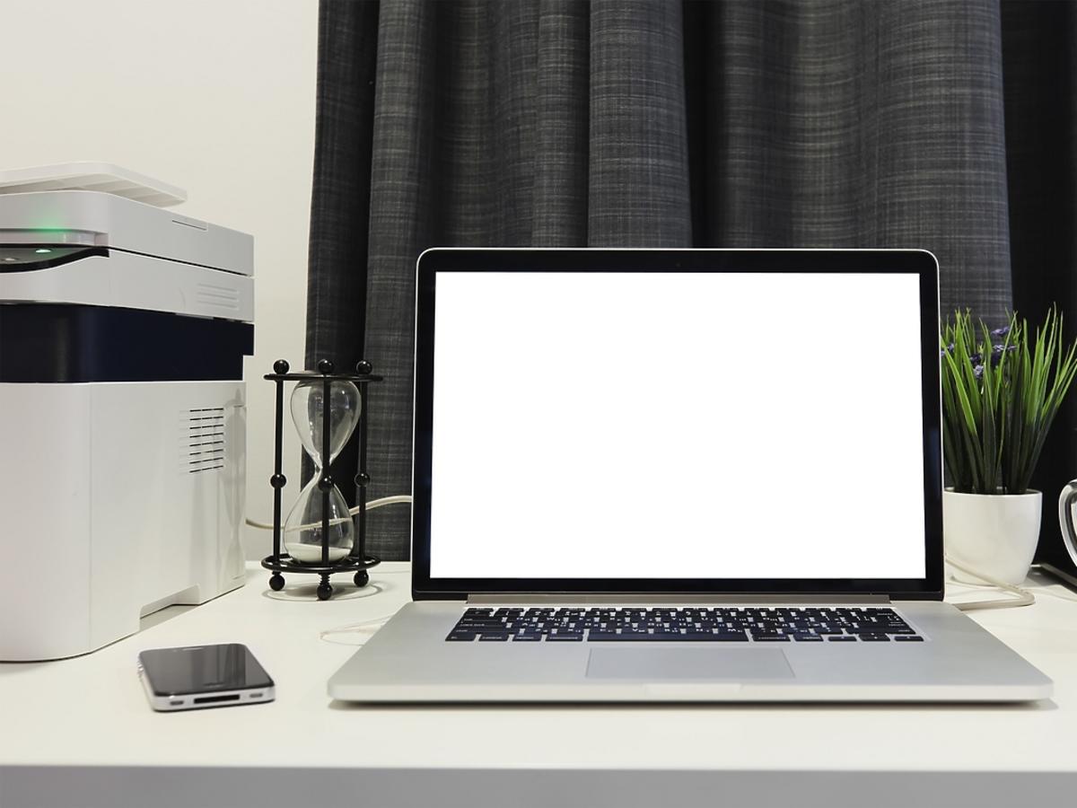 srebrny laptop, kubek z kawą, kwiatek, drukarka i kalendarz na białym biurku