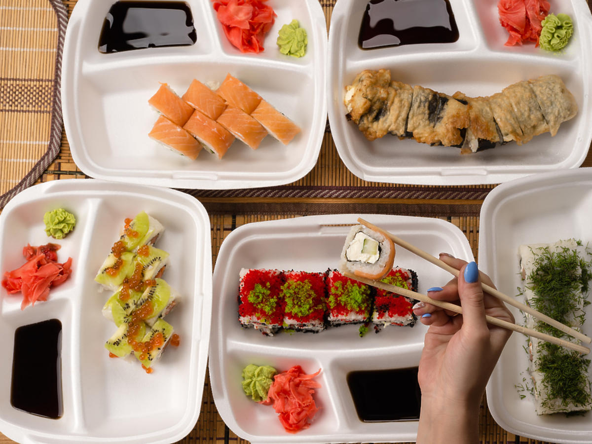 Stół zastawiony sushi i innymi przekąskami. Widoczne też pałeczki, którymi ktoś nabiera jedzenie.