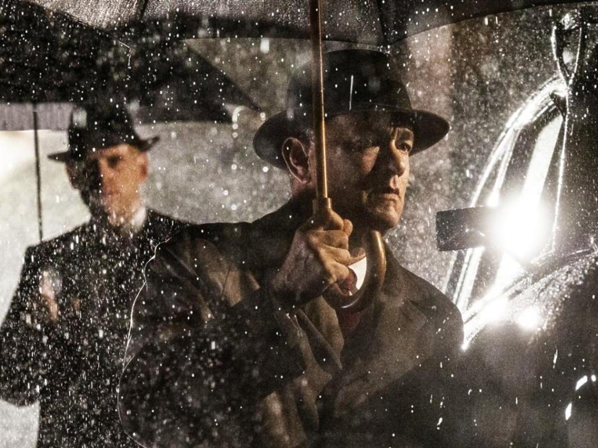 Tom Hanks w kapeluszu chroni się przed deszczem parasolem