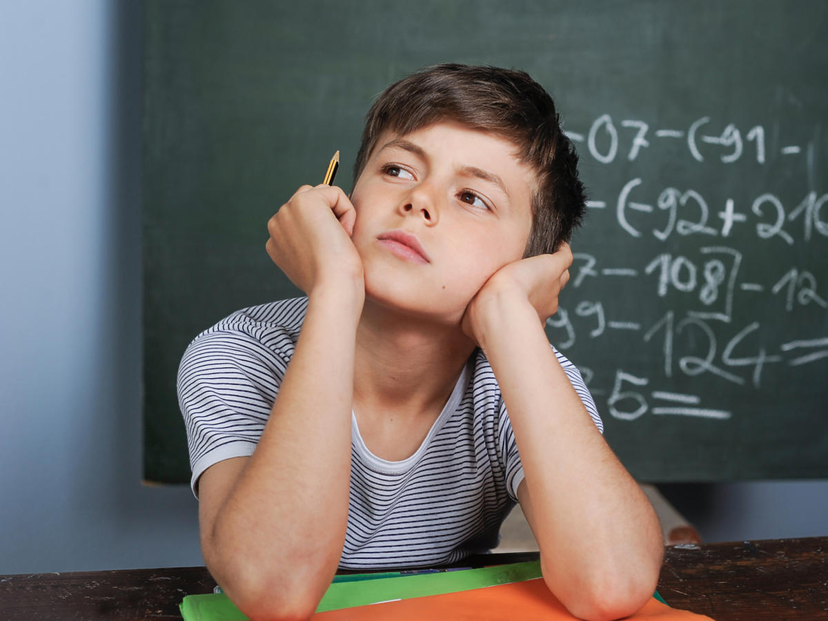 zamyślony chłopiec siedzący z tablicą szkolną za plecami